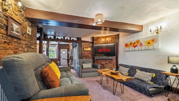 A cozy living room with a leather sofa, a wooden coffee table, and a TV mounted on a brick wall.