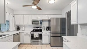 Una cocina moderna con armarios blancos, electrodomésticos de acero inoxidable, un ventilador de techo y un refrigerador grande.