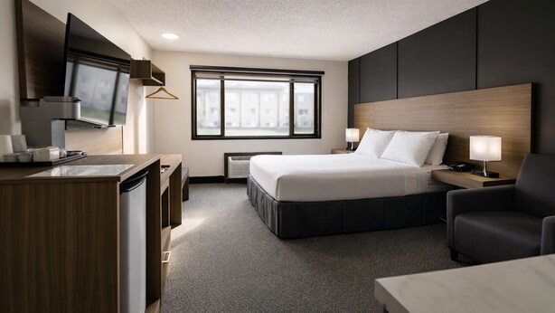 Una habitación de hotel con cama, escritorio, silla, televisión y ventana.