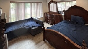 Une chambre à coucher avec un lit, une commode, un miroir et une fenêtre avec des stores.