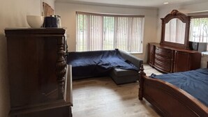 Une chambre à coucher comprenant un lit, une commode, un miroir, une fenêtre avec des stores et un luminaire au plafond.