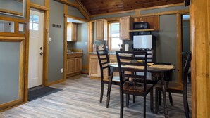 A kitchen with wooden cabinets, a dining table with chairs, a microwave, and a refrigerator. - Adorable 2-bedroom cabin with AC in charming Cheboygan (Cheboygan)
