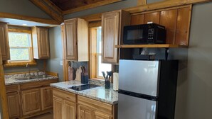 A kitchen with wooden cabinets, a stainless steel refrigerator, a microwave, and a sink. - Adorable 2-bedroom cabin with AC in charming Cheboygan (Cheboygan)