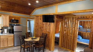 A cabin interior with a kitchen, dining area, and a sleeping area with a bunk bed. - Adorable 2-bedroom cabin with AC in charming Cheboygan (Cheboygan)