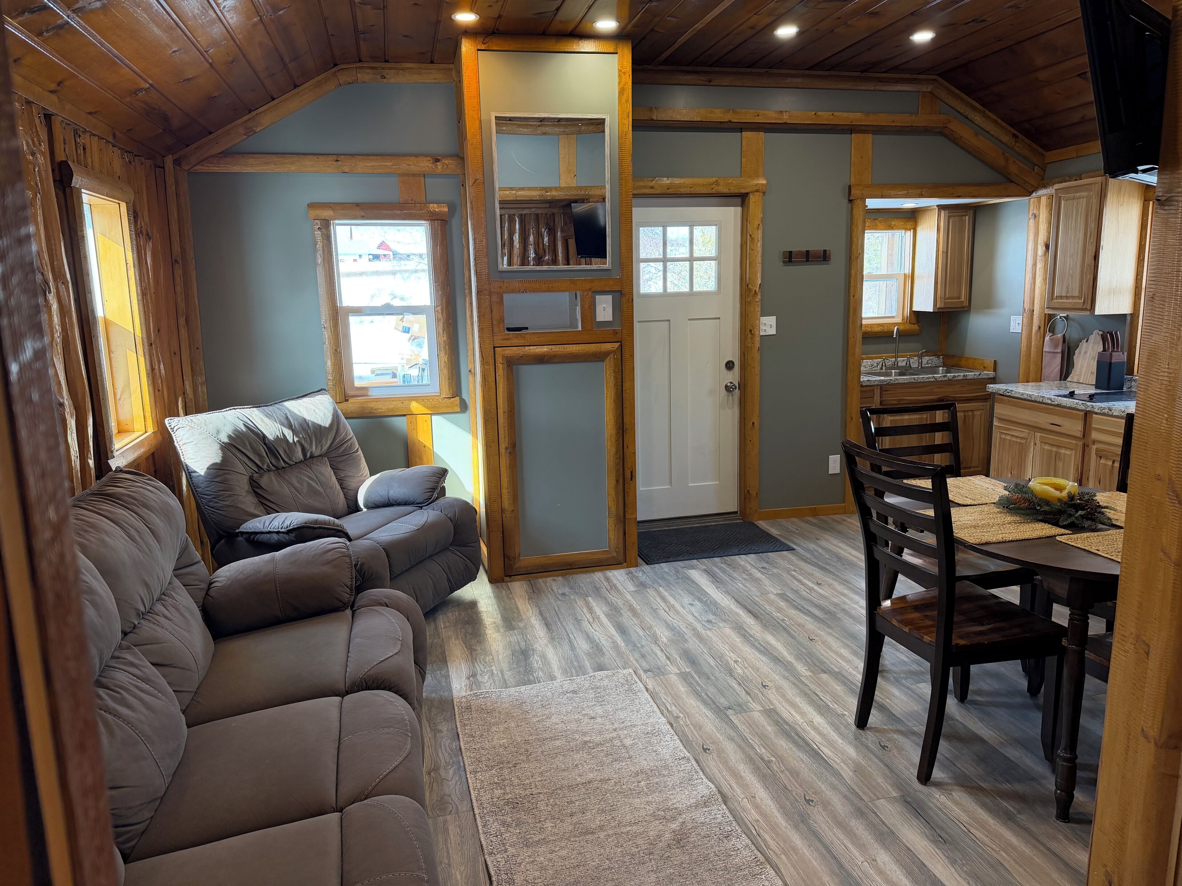 A cozy cabin interior with a sofa, dining table, kitchen area, and a door leading to a balcony.
