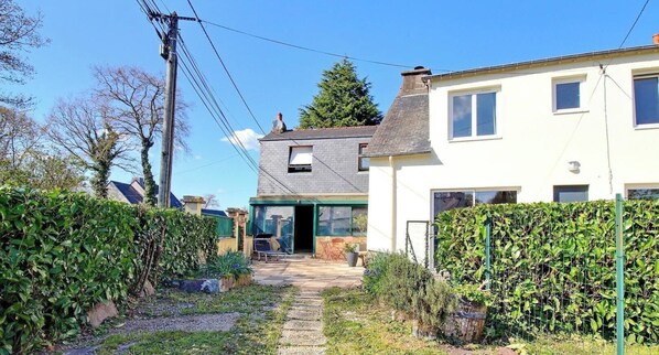 A residential property with a paved pathway leading to a front door, a visible chimney, and a garden area with various plants.