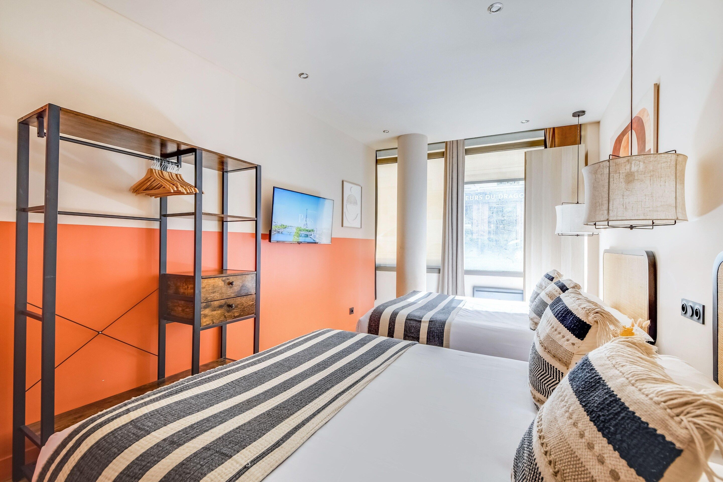 A hotel room with a bed, a hanging wardrobe, a television, and a window with curtains.