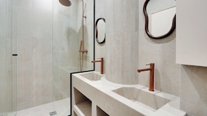 Un baño moderno con cabina de ducha de vidrio, dos lavamanos con grifos de cobre y un espejo grande.