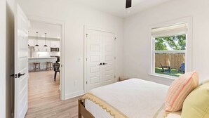 Un dormitorio con cama, ventana con vistas, puerta que da a una cocina y ventilador de techo.