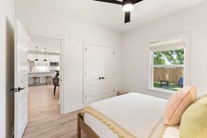 A bedroom with a bed, a window with a view, a door leading to a kitchen, and a ceiling fan. - Spacious 3 Bedroom Home Near Beaches and Shopping! (Pensacola)