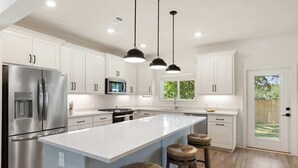 Una cocina moderna con armarios blancos, electrodomésticos de acero inoxidable, una isla grande e iluminación colgante.