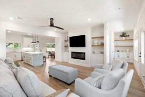 A modern living room with a sofa, ottoman, and a flat-screen TV mounted on the wall. - Spacious 3 Bedroom Home Near Beaches and Shopping! (Pensacola)