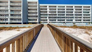 Ein mehrstöckiges Hotel mit Balkonen, einer Promenade, die zum Strand führt, und blauem Himmel.