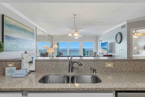 A modern kitchen with granite countertops, a stainless steel sink, and a large mirror reflecting the room. - Islander E 7011, Stunning oceanfront condo (Fort Walton Beach)