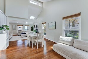 A spacious living area with a dining table, white furniture, and large windows. - Croatan Beach Spacious 4BR Home with Views (Virginia Beach)