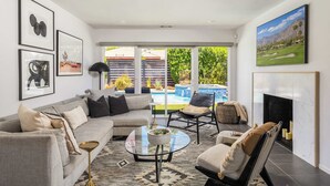 A living room with a sofa, armchairs, a glass coffee table, and a fireplace. - Palm Springs Mid-Century Home | Pool, Spa, Casita + Sweeping Mountain Views (Palm Springs)