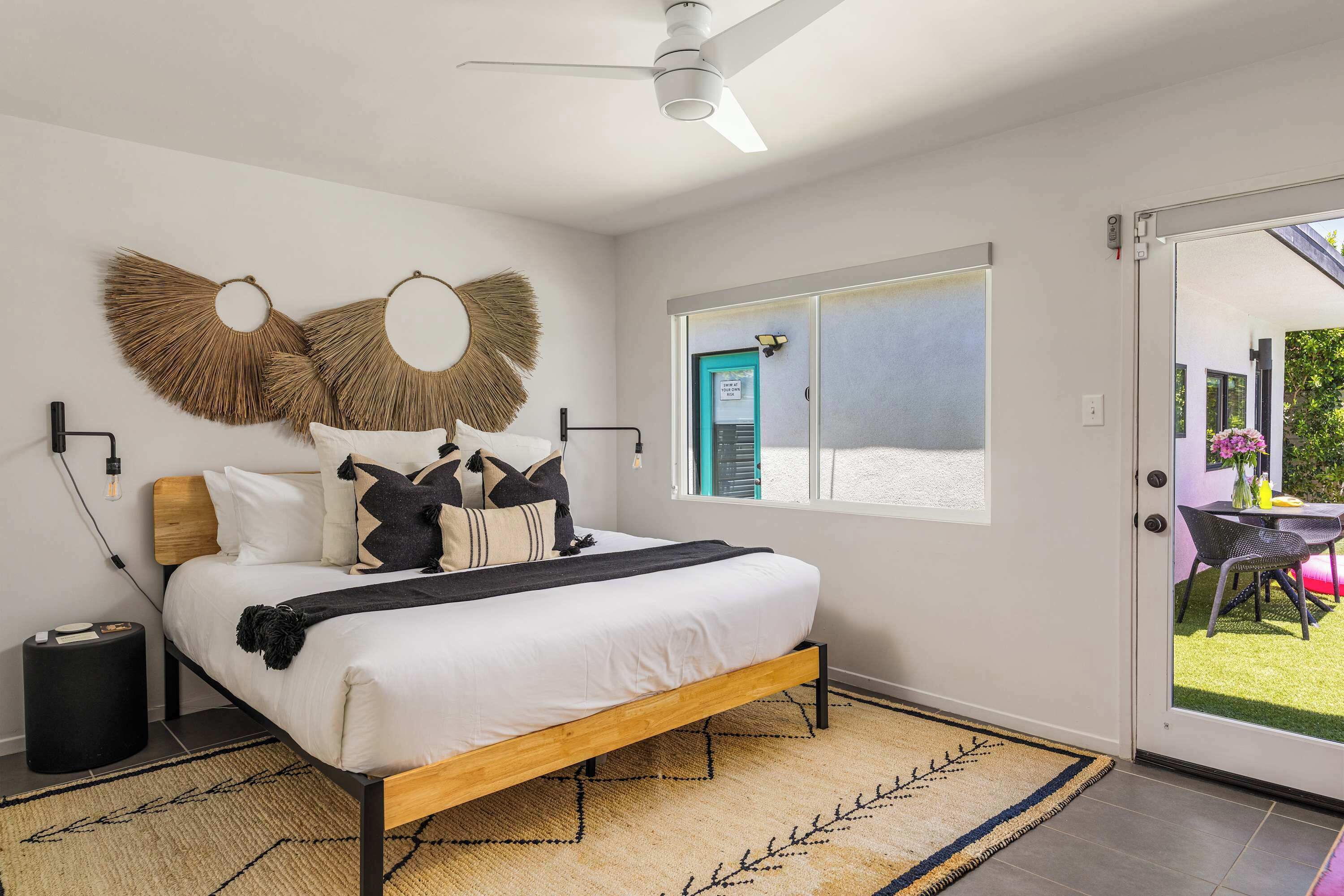 A bedroom with a bed, a ceiling fan, a window, and a door leading to an outdoor area.