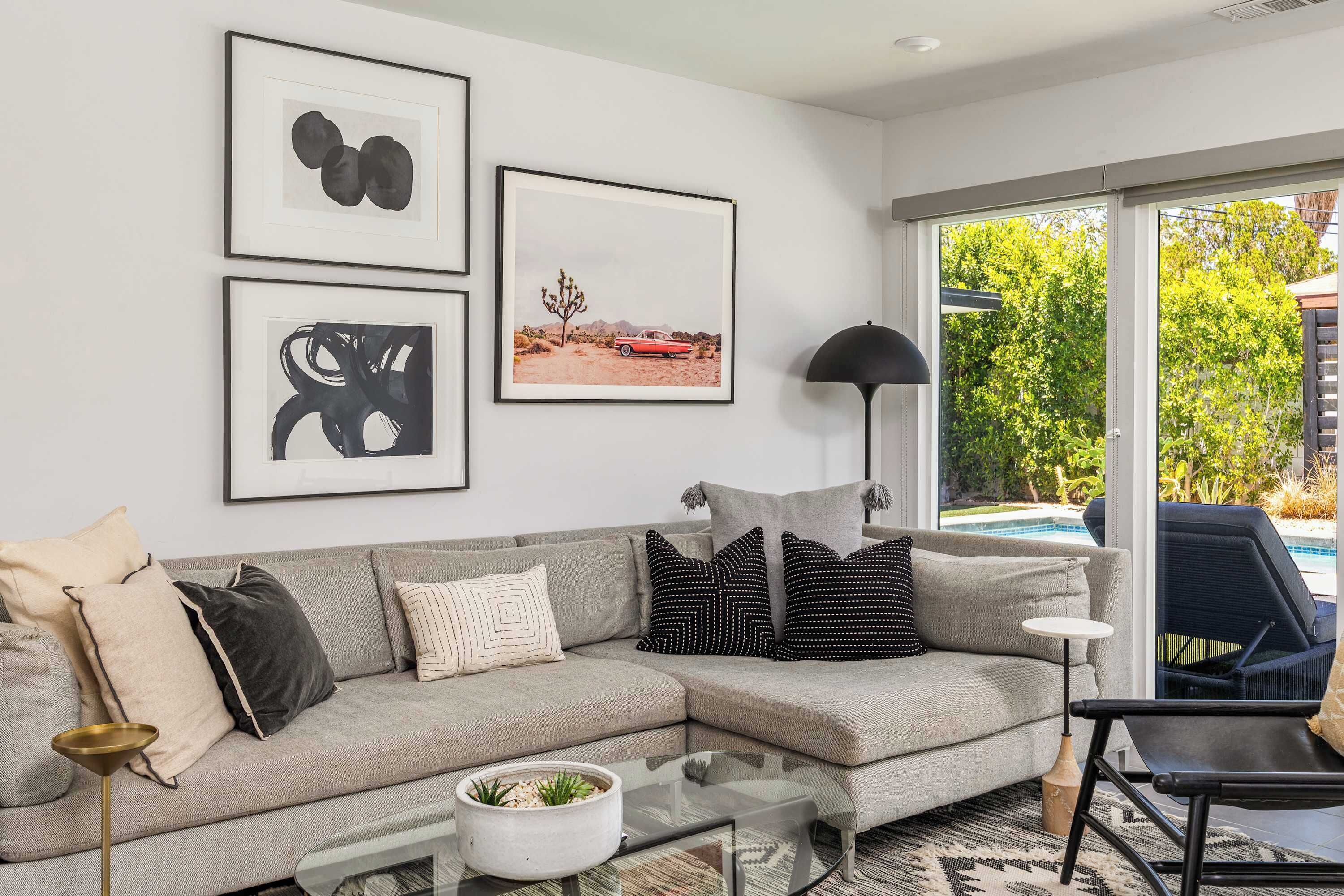 Ein modernes Wohnzimmer mit einem grauen Ecksofa, einem Glastisch und Blick auf einen Pool.