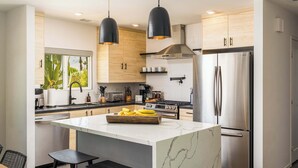A modern kitchen with a marble island, stainless steel appliances, and black pendant lights. - Palm Springs Mid-Century Home | Pool, Spa, Casita + Sweeping Mountain Views (Palm Springs)