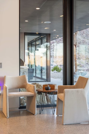 A modern interior with two sofas, a small table, and a large window with a view of a rocky landscape. - Palm Desert Mountaintop Estate | Lap Pool & Spa, Valley Views & Outdoor Kitchen (Palm Desert)