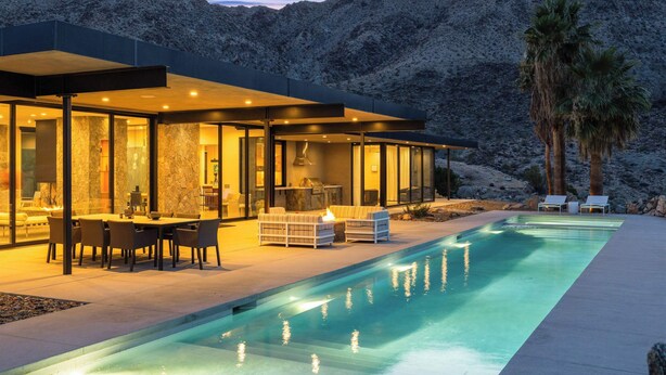 Una casa moderna con piscina, mobiliario de exterior y montañas al fondo.