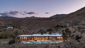 Una casa moderna con piscina, rodeada de terreno rocoso y montañas.