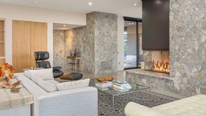 Un salón moderno con chimenea de piedra, mobiliario de cuero y una mesa de centro de cristal.
