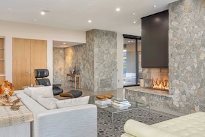 A modern living room with a stone fireplace, leather furniture, and a glass coffee table. - Palm Desert Mountaintop Estate | Lap Pool & Spa, Valley Views & Outdoor Kitchen (Palm Desert)