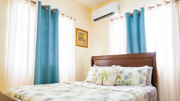 Una cama con cubrecama floral, cabecera de madera y cortinas azules.
