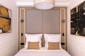 Une chambre d’hôtel avec un grand lit, deux tables de chevet, un luminaire au plafond et des œuvres d’art accrochées aux murs.