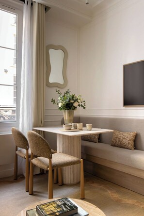Une pièce moderne avec une table ronde, deux chaises, un canapé, un miroir et un vase rempli de fleurs.