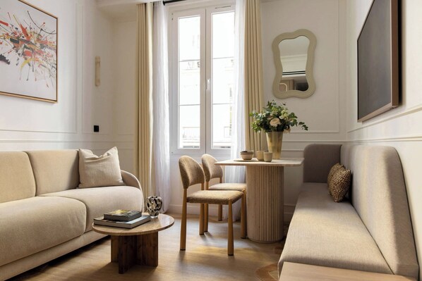 Un salon avec un canapé, des fauteuils, une table basse, un vase de fleurs et un tableau accroché au mur.