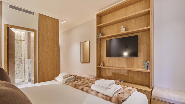 A hotel room with a bed, a TV mounted on a wooden shelf, a mirror, and a door leading to a bathroom. - Luxurious Airconditioned Apartment Arc de Triomphe (Paris)