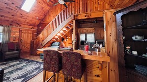 L’intérieur d’une cabane en bois comprend une cuisine, un coin repas et un escalier menant à un étage supérieur.