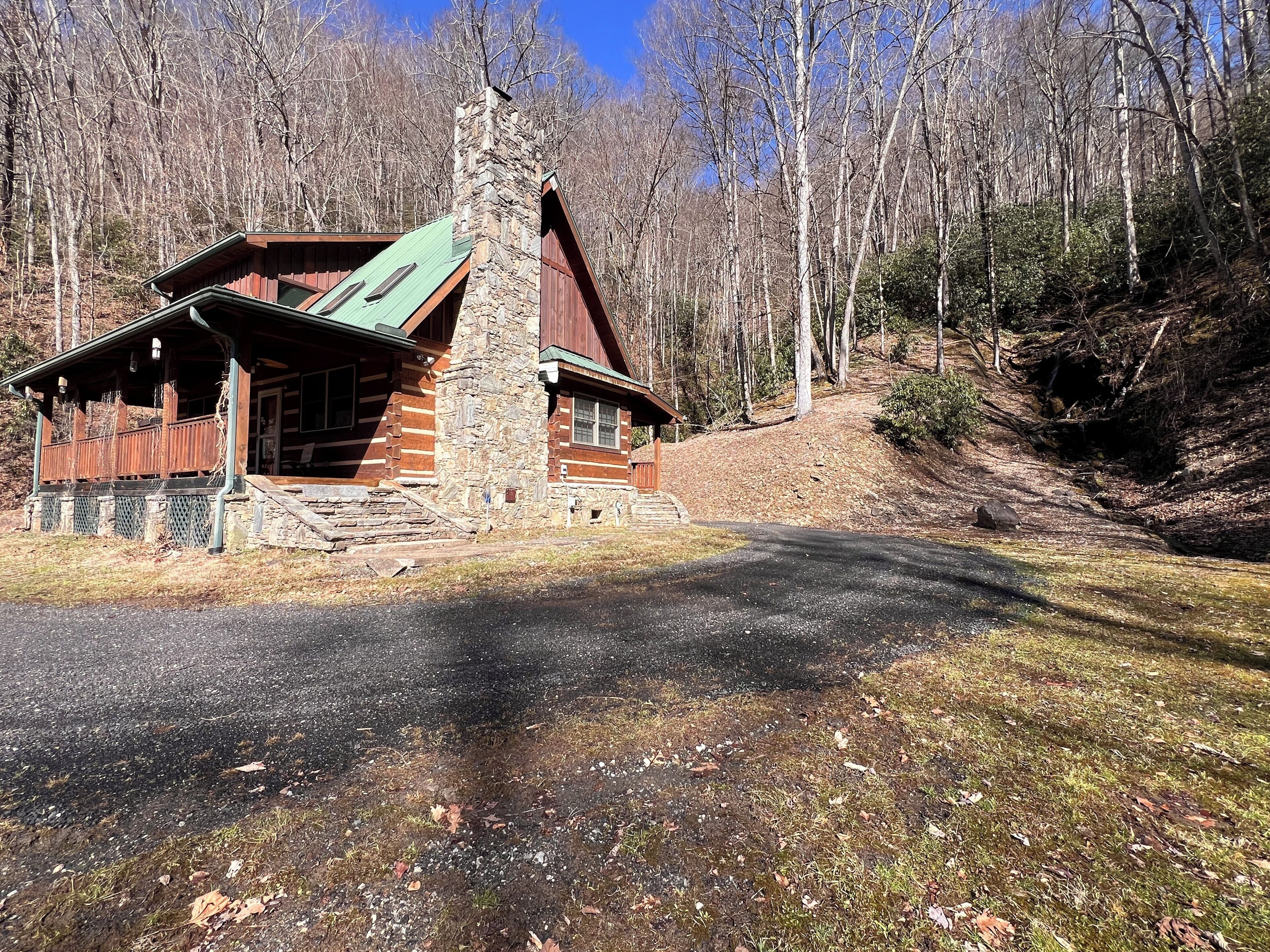 A log cabin with a stone chimney, a porch, and a view of the surrounding forest.
