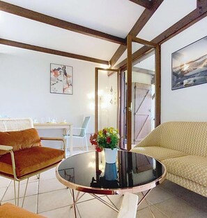 Ein Zimmer mit einem runden Glastisch, zwei Stühlen, einer Couch, einer Essecke mit weißem Tisch und Stühlen sowie einem großen Spiegel.