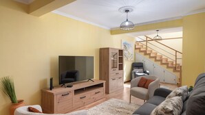 Ein Wohnzimmer mit Fernseher, Holzschrank, Sofa und Treppe.