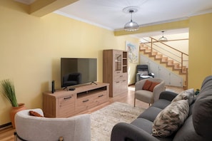 Een woonkamer met een televisie, een houten kast, een bank en een trap.