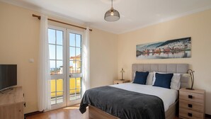 Ein Schlafzimmer mit Bett, Nachttischen, einem Fernseher, einem Gemälde und Blick durch eine Glastür.