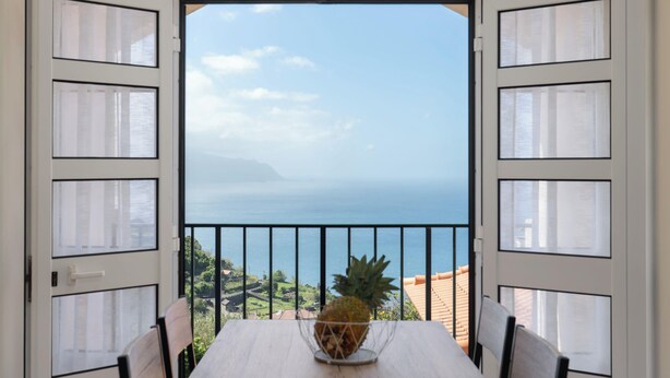 Ein Balkon mit Tisch und Stühlen, eine Ananas auf dem Tisch und Blick aufs Meer.
