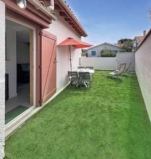 Ein Garten mit Kunstgrasanlage, einem Tisch mit Stühlen und einem roten Sonnenschirm.