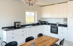 A modern kitchen with white cabinets, a wooden dining table, and a chandelier.