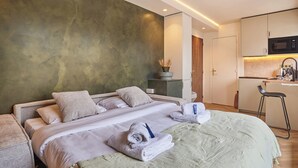 Quarto de hotel moderno com cama, pequena cozinha e banheiro.