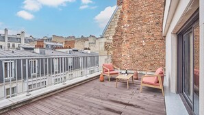 Terraço no telhado com parede de tijolos, piso de madeira e duas cadeiras cor-de-rosa com uma mesa pequena.