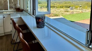 Una cocina con un ventanal grande, una encimera blanca y vistas a un viñedo.