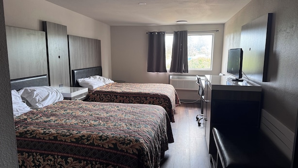 Una habitación de hotel con dos camas, un escritorio, un televisor y una ventana con cortinas.