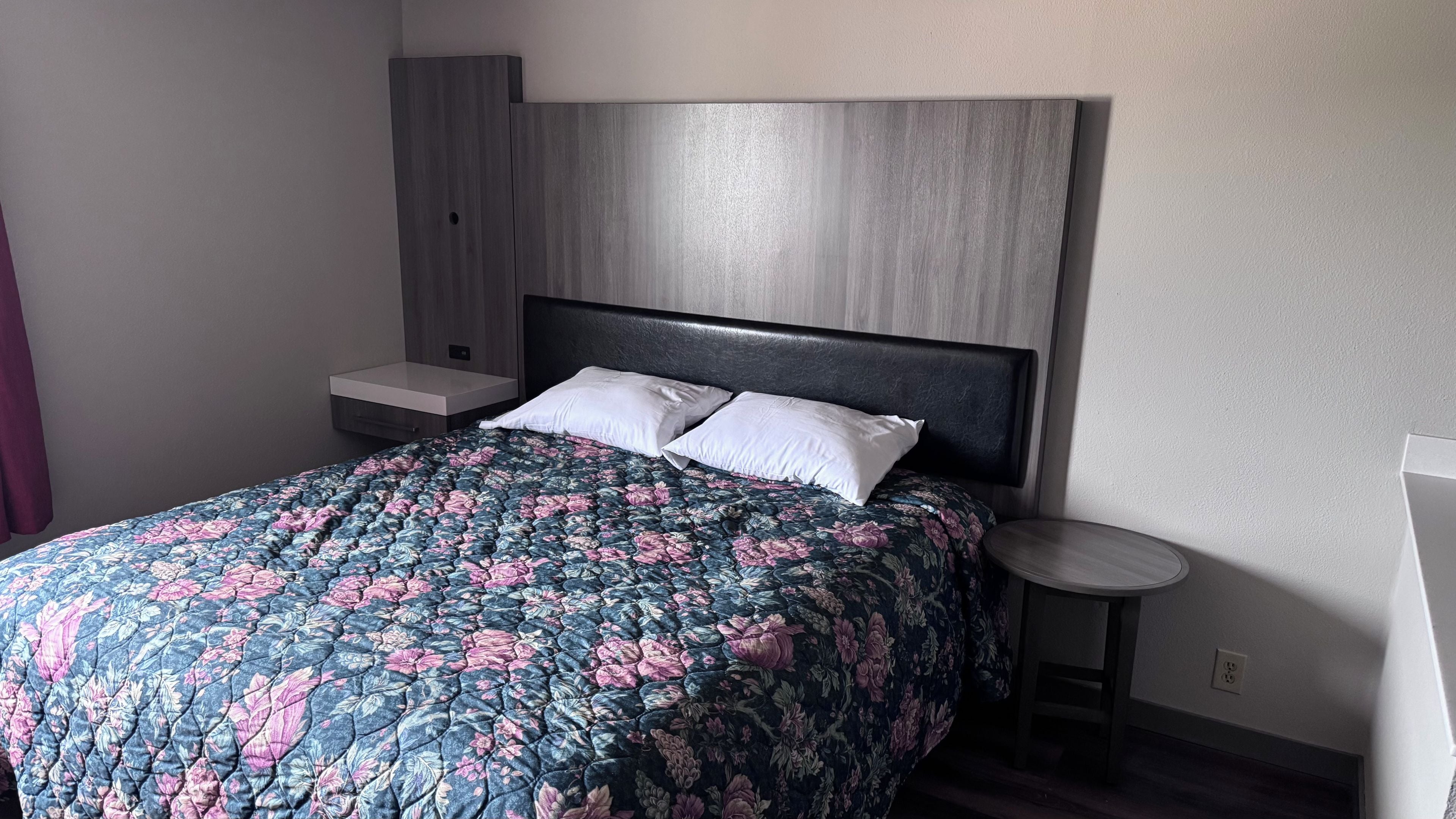 Quarto com cama, duas mesas de cabeceira e uma mesinha redonda.