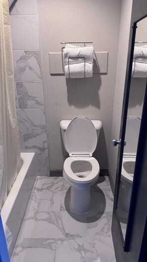 A bathroom with a toilet, a towel rack, and a bathtub. - Midway Inn (Bremerton)