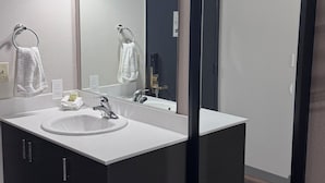 Un baño con un lavamanos blanco, gabinetes oscuros, un espejo grande y un perchero para toallas.