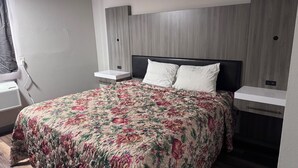 Una habitación de hotel con cama, mesitas de noche, estante en la pared y ventana con cortinas.